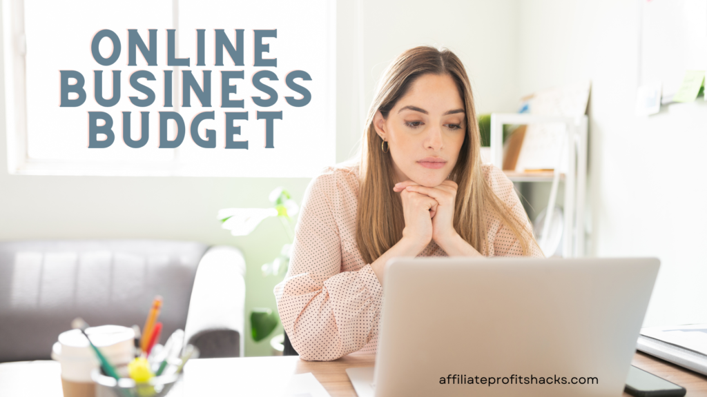 A thoughtful woman sits at her desk, gazing at a laptop with "ONLINE BUSINESS BUDGET" text in large letters on the wall behind her and a website URL "affiliateprofitshacks.com" at the bottom of the image.