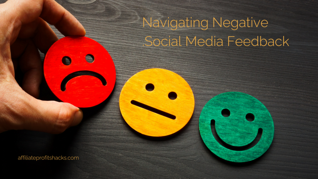 "A human hand holding a red sad face emoticon, with a neutral yellow emoticon and a happy green emoticon lying on a dark wooden surface. Text 'Navigating Negative Social Media Feedback' with a URL 'affiliateprofitshacks.com' above."